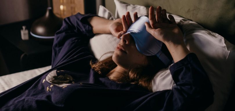 Woman lying awake in bed at night with a sleep mask