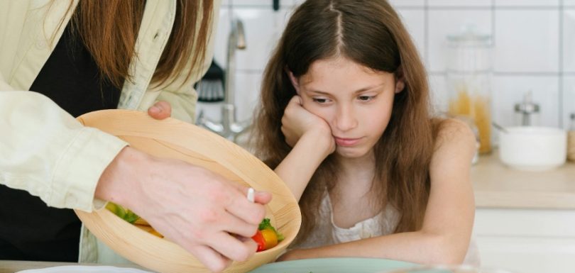 Parent serving vegetables to a child who appears uninterested in eating