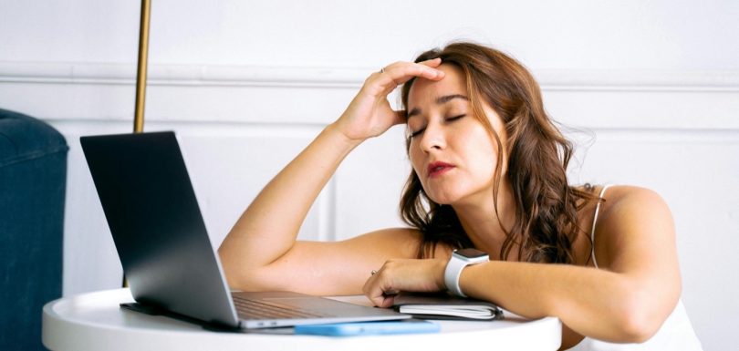 Tired woman sitting at a laptop with her hand on her forehead