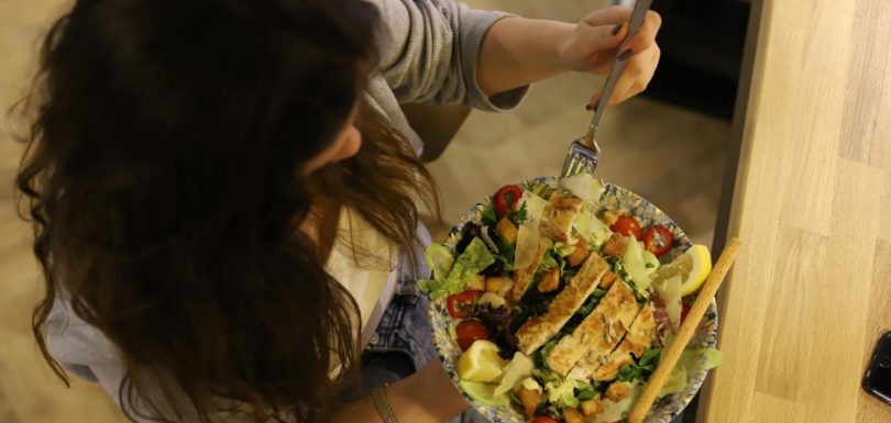 Woman eating a balanced meal with grilled chicken, salad, tomatoes, avocado, and bread