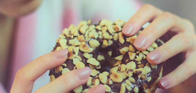 Person holding a chocolate-covered donut topped with chopped nuts