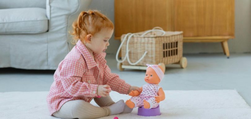 Young child sitting with a baby doll and toy potty at home