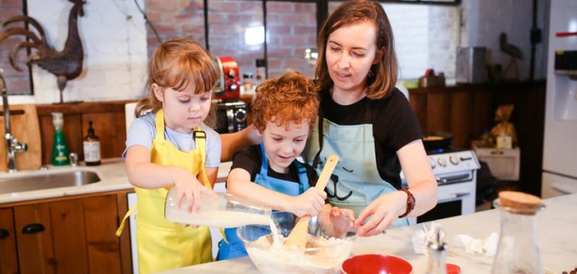Parent cooking with two young children in the kitchen