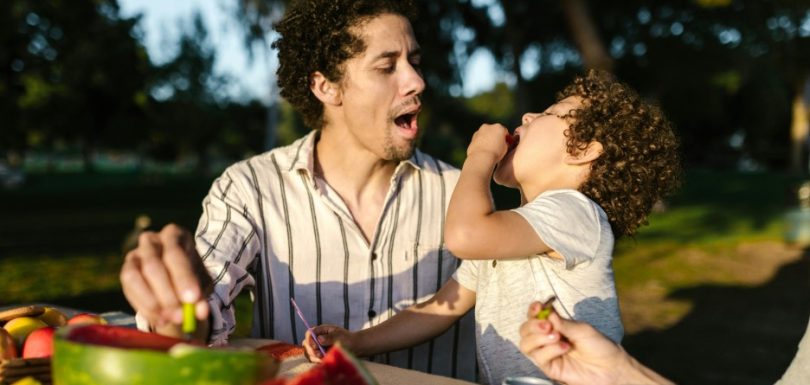 Parent and young child eating fresh fruit together outdoors